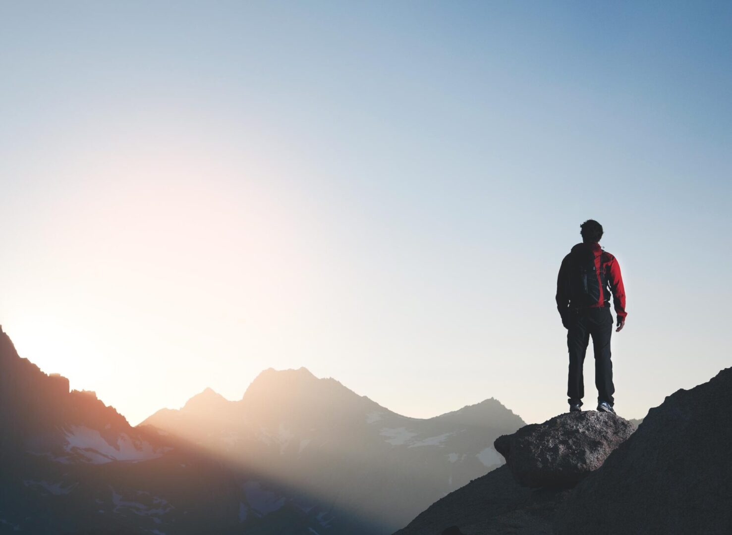 Hiker silhouetted on rock overlooking mountain sunrise